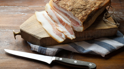 2GABY13 Guanciale Amatriciano with cutting board and knife on wooden table. The guanciale is a pork sausage typical of central Italy. Close-up, space for text
