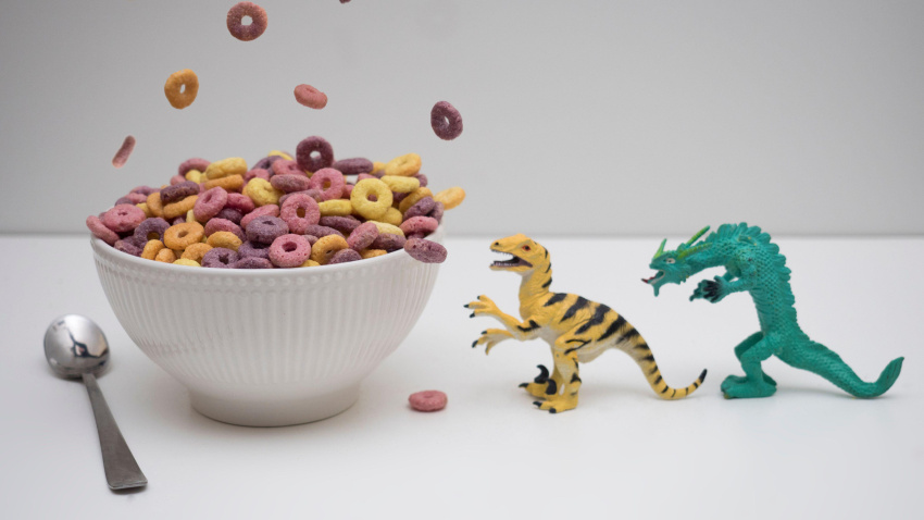 2GAHNJD Colorful breakfast cereal for kids falling on top of white bowl with dinosaurs