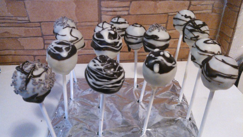 El chocolate es delicado.Tiene sus tiempos y sus temperaturas, así que no te saltes ningún paso.Sacamos los cake pops de la nevera 5 minutos antes de bañarlos para que se atemperen. Es impoortante, porque si hay mucho contraste de temperatura, se cuarteará la cobertura al enfriar.Ve con calma y sin prisa. Puedes bañarlos usando una cuchara o meterlos en el bol directamente, siempre en horizontal y dando vuelta muy lentamente, hasta que la bolita quede cubierta. En cuanto deje de gotear, está listo. Déjala secar en un vaso alto para que no se caiga. Antes de que se sequen del todo puedes echarles topings, fideos, perlitas o lo que más te guste.En cuanto les pilles el truco es fácil hacerlos y están riquísimos. Cake pops de chocolate
