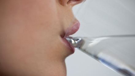 CX6K7Y A young woman drinking a glass of water, close up of mouth