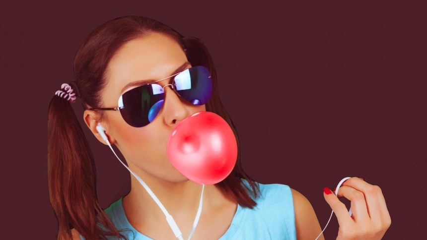 G0C777 Beautiful funny model girl wearing sunglasses with bubble of chewing gum listens to the music (white earphones)